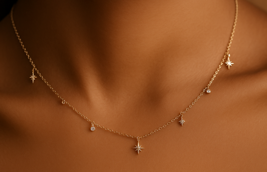 Collier doré minimaliste porté autour du cou d’une femme à la peau caramel, avec pendentifs étoiles et pierres fines, éclairé par une lumière douce