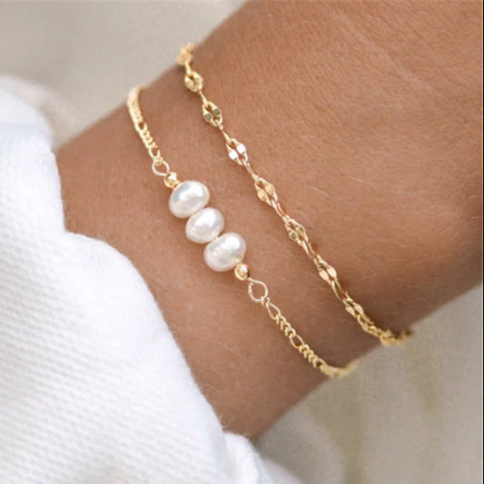 bracelet doré avec trois perles blanches sur un poignet
